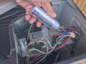 HVAC technician reaching for AC capacitor during replacement process